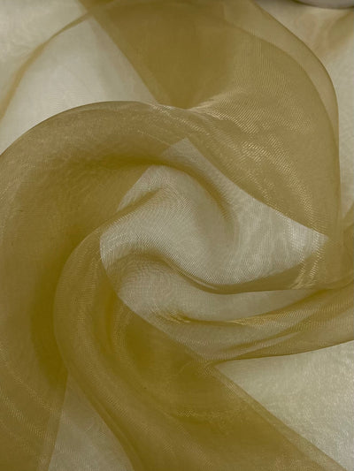 Here's a rephrased version using the given product data:
A close-up of the "Organza - Sand - 150cm" from Super Cheap Fabrics reveals its sheer, golden texture with a smooth, flowing form. This polyester material gently swirls into soft and elegant patterns while light and shadows dance across its delicate surface.
