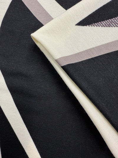 Close-up of Super Cheap Fabrics' Viscose Knit - Curve (145cm): two overlapping breathable stretch fabrics with abstract black, white, and taupe geometric angular patterns.