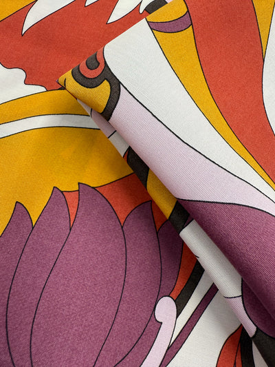 Close-up of Super Cheap Fabrics' Printed Viscose - Fantasia (145cm), a lightweight fabric featuring a vibrant abstract floral pattern in yellow, orange, purple, and white with bold shapes and black outlines.