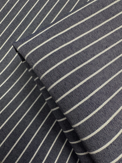 Close-up of Super Cheap Fabrics' Chambray - Naval Academy - 150cm, a lightweight dark blue fabric with thin white stripes. Two layered pieces create intersecting lines and a textured pattern reminiscent of the Naval Academy color.