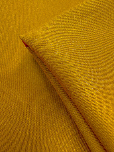 A close-up of Stretch Denim - Mustard - 150cm by Super Cheap Fabrics shows its smooth, tightly woven texture and neatly folded section. This medium weight, durable denim offers vibrant color and a comfortable stretch.