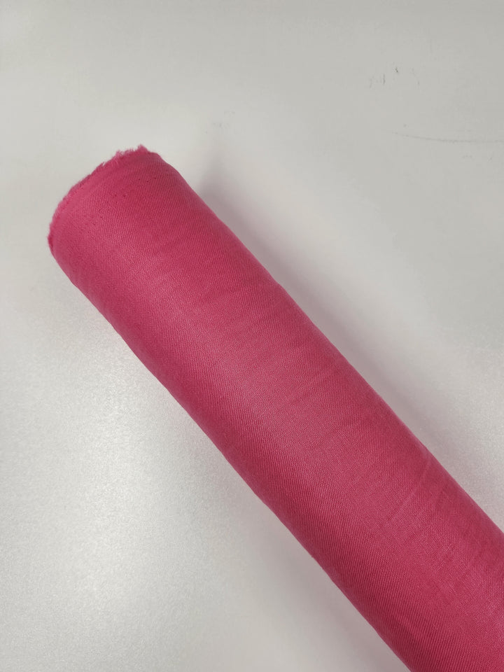 A rolled-up bolt of Pure Washed Linen in hot pink from Super Cheap Fabrics is placed on a white surface, measuring 140cm in width.