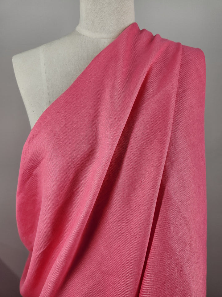 A mannequin adorned with Super Cheap Fabrics' Pure Washed Linen in Hot Pink, a soft and textured fabric that envelops the form in a flowing manner, highlighting its vibrant color and smooth lines. Set against a plain, neutral background, the linen's elegance truly stands out.