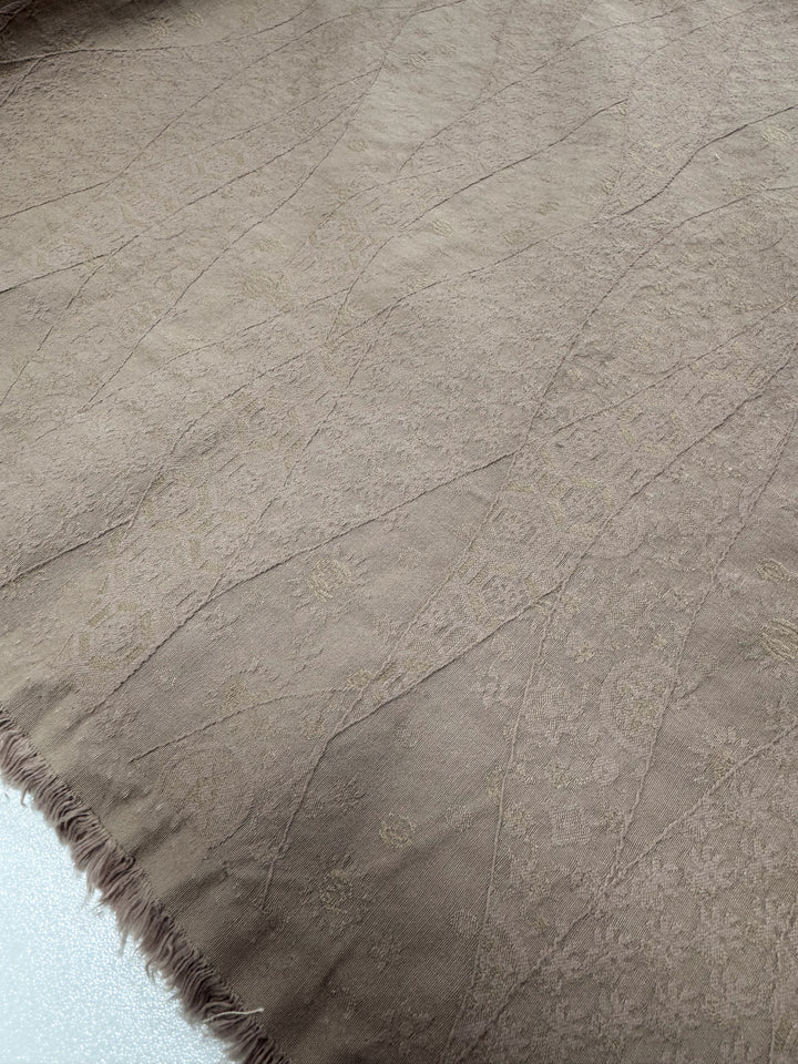Close-up of Super Cheap Fabrics' "Stretch textured Bengaline - Dune" in beige, showcasing its subtle floral patterns. Featuring a bordered fringe on the left and light intersecting lines, this 150cm polyester fabric is ideal for unique clothing accessories.