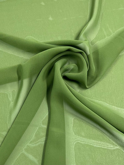 The Hi-Multi Chiffon - Campsite by Super Cheap Fabrics, a sheer green 100% polyester piece, is artfully folded and gathered for a textured flow. This lightweight 150cm fabric lays flat, highlighting its translucent elegance.