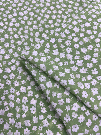 The Super Cheap Fabrics' Salt Shrunk Print - Jassy, 155cm, showcases a green backdrop with small white flowers. Expertly crafted with gentle folds, this design offers a charming depth.