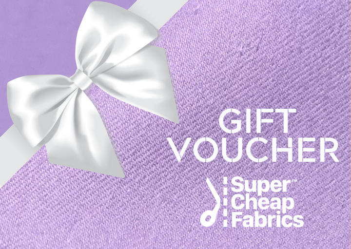 A Super Cheap Fabrics Gift Vouchers gift card with a lavender background. The left side showcases a large white satin bow. Text reads: "GIFT VOUCHER Super Cheap Fabrics." The design features a textured fabric pattern, perfect for any sewing enthusiast looking to redeem online.