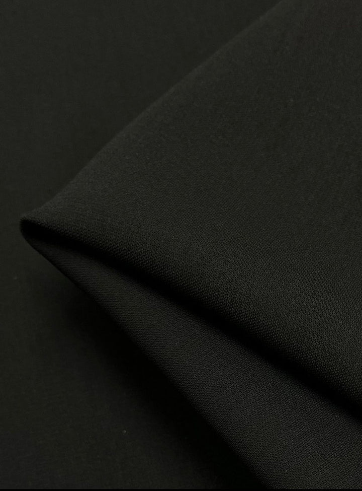 Close-up of the Stretch Crepe - Raven by Super Cheap Fabrics, showcasing its smooth, folded black fabric with an elegant matte finish, forming a sharp corner against a dark background.