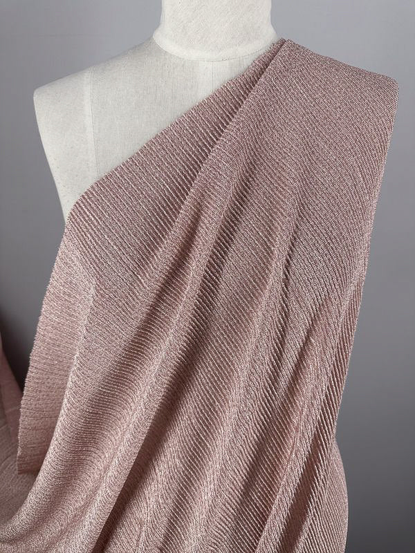 A mannequin showcases the Metallic Knit - Blush - 150cm from Super Cheap Fabrics, featuring a textured, one-shoulder draped stretch material. The fine ribbed pattern enhances the graceful flow over the form, while the neutral background highlights the fabric's blush color and texture.