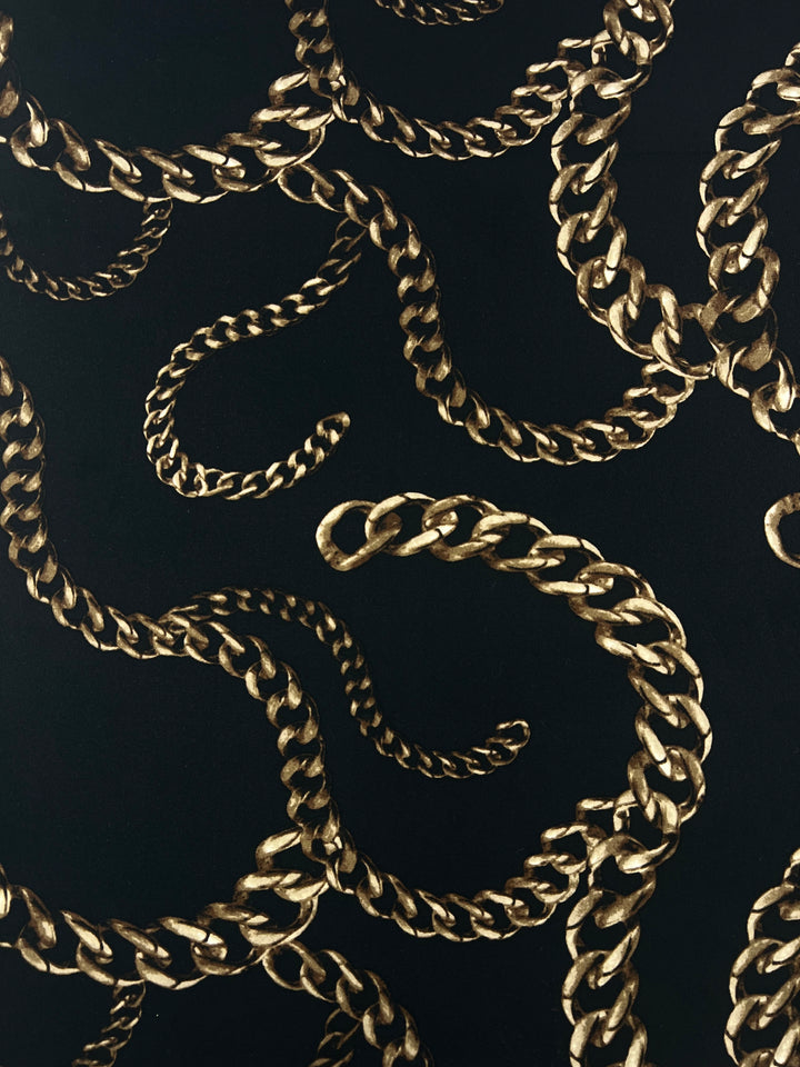 A pattern of intricately intertwined gold chains set against a black background. The chains form looping and curling shapes on a medium weight polyester spandex fabric, creating a dynamic and luxurious visual effect, Super Cheap Fabrics' Printed Lycra - Chains - 150cm.