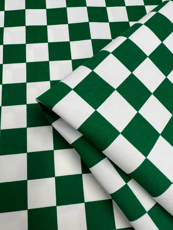 A close-up of folded fabric with a green and white checkered pattern. The squares are uniformly sized, creating a bold, repetitive design. The Cotton Drill - Green Chess - 155cm by Super Cheap Fabrics appears to be of heavy, textured material, neatly arranged.