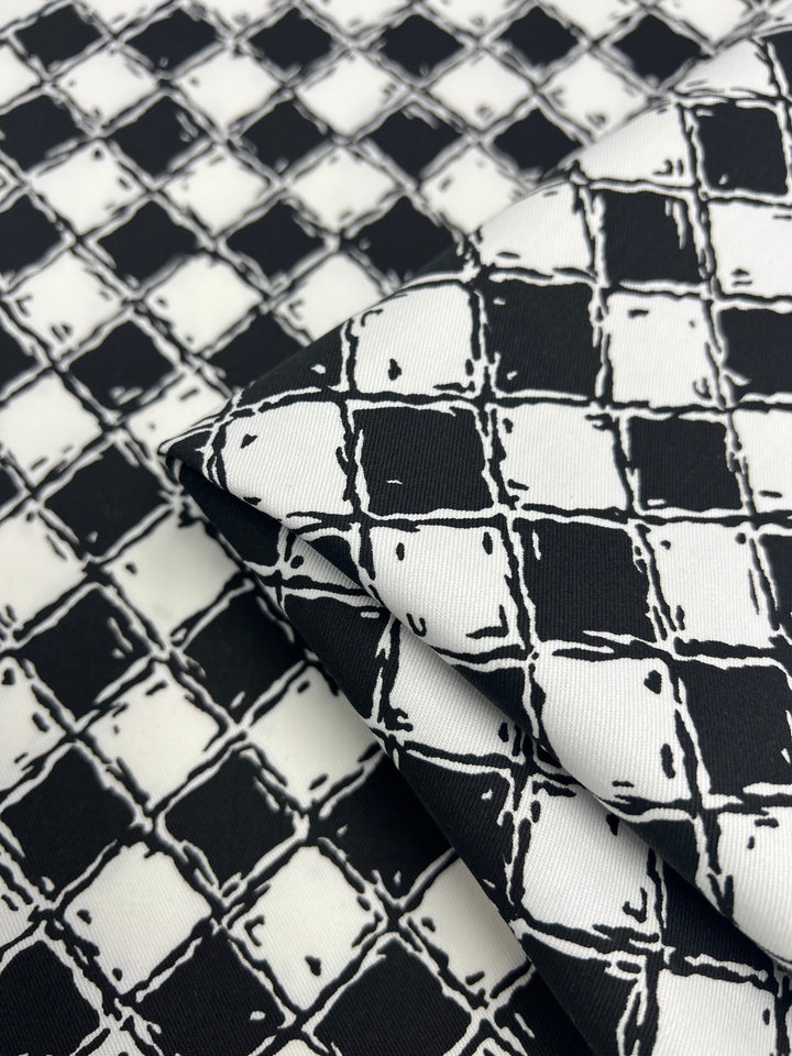 Close-up of a folded piece of fabric featuring a black and white checkered pattern with a slightly irregular, hand-drawn look. The Super Cheap Fabrics Cotton Drill - Mosaic - 155cm has evenly spaced squares creating a grid-like design, while its durable diagonal weave adds an intriguing texture.