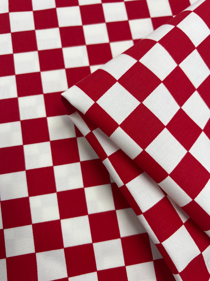 A close-up image of **Super Cheap Fabrics Cotton Drill - Red Chess - 155cm**, folded neatly. Made from 100% cotton, the pattern consists of a series of evenly spaced squares in alternating colors, giving it a classic, vibrant appearance.