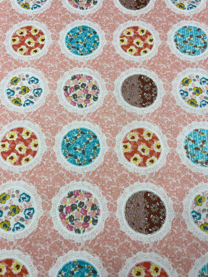 A patterned fabric with a repeating design of circular floral motifs perfect for children's dresses. Each circle contains a different floral print, surrounded by white lace-like borders, set against a pink textured background. The floral prints vary in color, including blue, yellow, and red. This is the Printed Cotton - Pink Mixed Mirrors - 112cm by Super Cheap Fabrics.