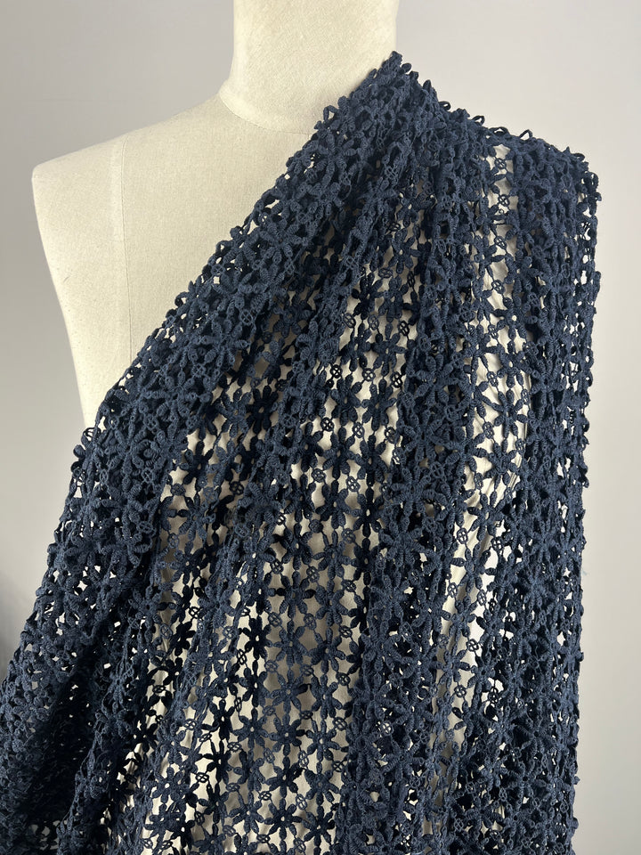 Close-up of a mannequin draped in Super Cheap Fabrics' Anglaise Lace - Navy - 127cm. The lace fabric features an intricately crocheted floral openwork pattern, creating a delicate appearance. The image highlights the detailed craftsmanship and texture of the lace, ideal for bridal wear or elegant home décor.