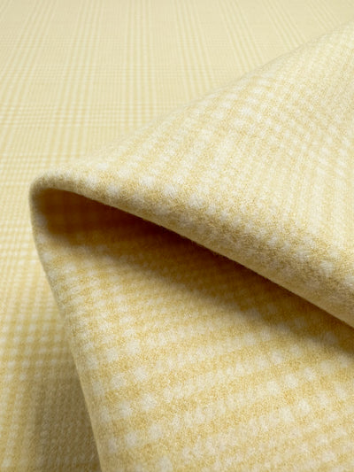 Close-up of the Super Cheap Fabrics' Wool Flannel - Limon, measuring 148cm. This soft, folded, heavyweight yellow wool blend fabric has a subtle checked pattern and offers a smooth, plush texture for warmth and comfort.