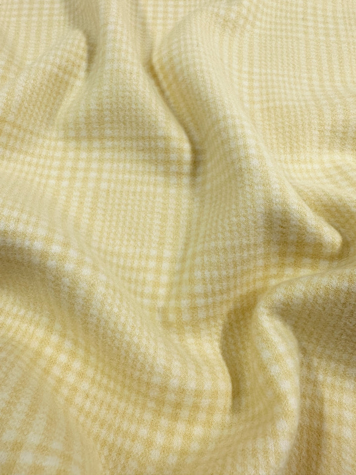 Close-up of Super Cheap Fabrics' Wool Flannel - Limon, showcasing its soft yellow and white plaid pattern with a textured surface. This cozy wool blend drapes elegantly, forming smooth waves and folds. Width: 148cm.