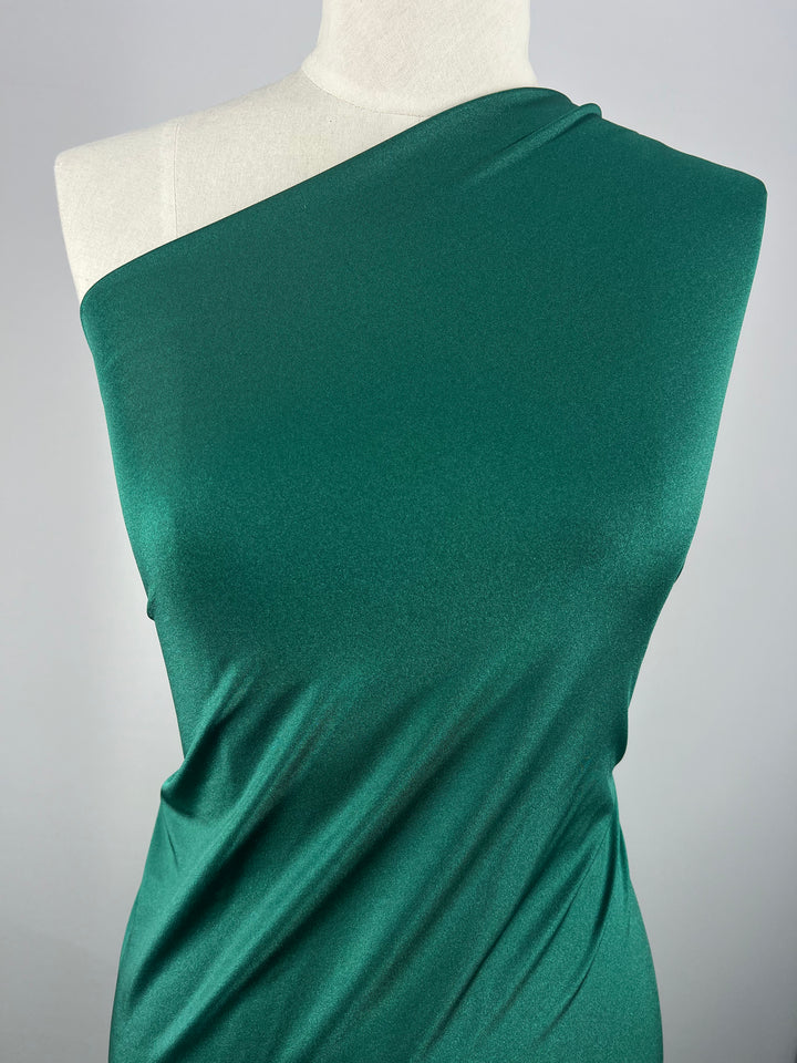 A mannequin displays an elegant green jacket, showcasing the smooth nylon lycra fabric from Super Cheap Fabrics. The jacket drapes gracefully with its four-way stretch, highlighting its simple yet sophisticated design against a plain, neutral background.