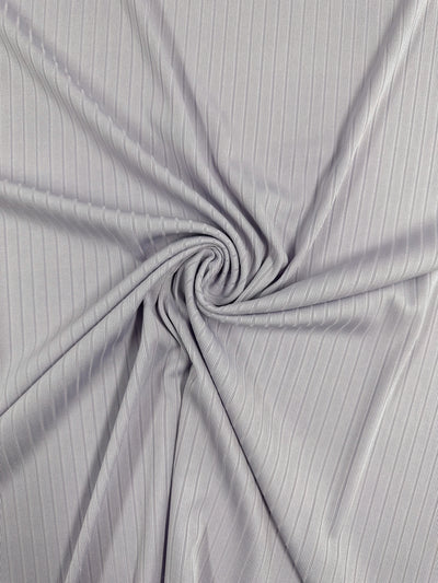 Close-up of the Rib Knit - Thistle by Super Cheap Fabrics, featuring a light gray shade with textured pinstripes. The stretchy 175cm fabric is elegantly twisted into a spiral, forming dynamic folds and shadows.