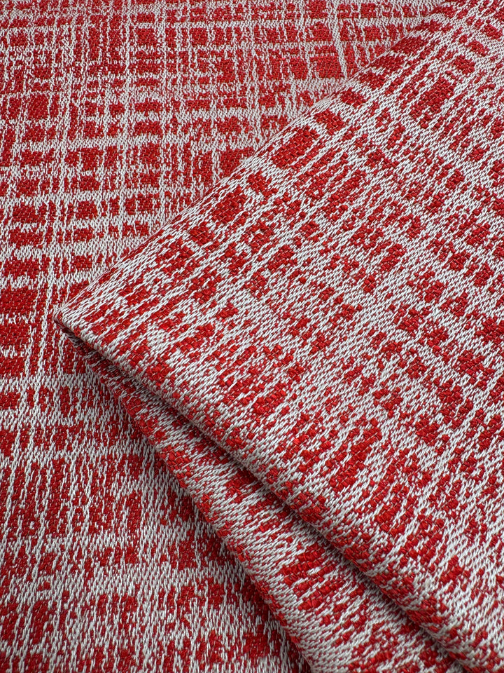 Red and white textured Dexter 35 fabric, reminiscent of Montpellier 26, features an abstract crosshatch pattern. This heavy upholstery fabric from Super Cheap Fabrics is folded in front, with a flat section beneath displaying a geometric design. Width: 147cm.