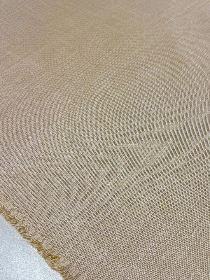 A close-up of the Upholstery - Rhodes Natural from Super Cheap Fabrics shows a heavy weight fabric with a subtle woven texture in light beige. The smooth acrylic-cotton blend ensures durability, while slightly frayed edges add character. Measures 144cm wide.