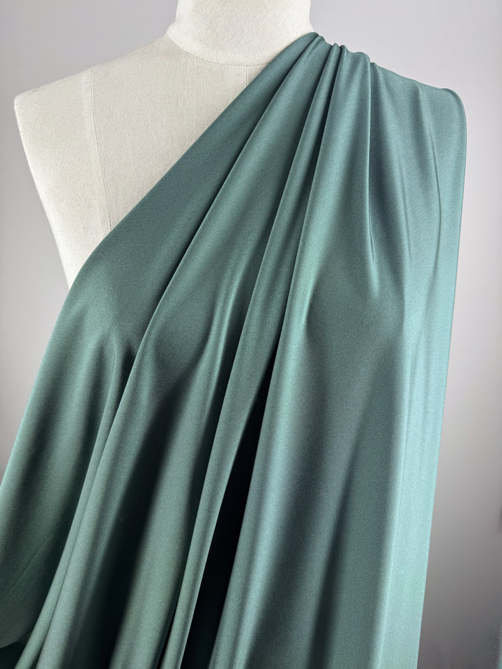 A close-up of a mannequin showcases Super Cheap Fabrics’ Nylon Lycra - Bistro Green (154cm), elegantly draped over one shoulder in smooth, flowing folds against a plain light background.