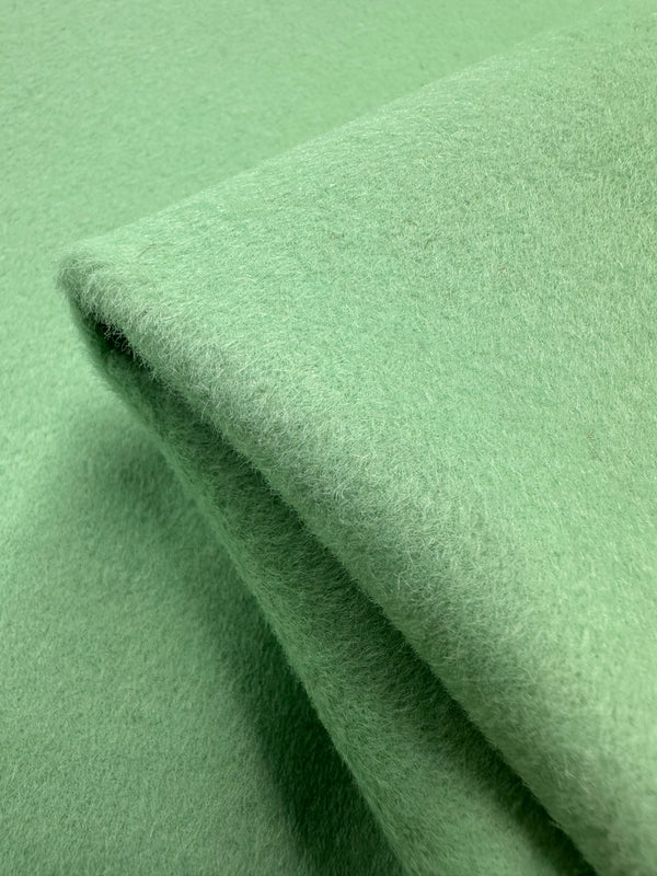 Close-up of Super Cheap Fabrics' Wool Cashmere - Green Ash - 157cm, showcasing its luxurious softness and fuzzy texture with folded layers. This plush, light green fabric looks warm and inviting.