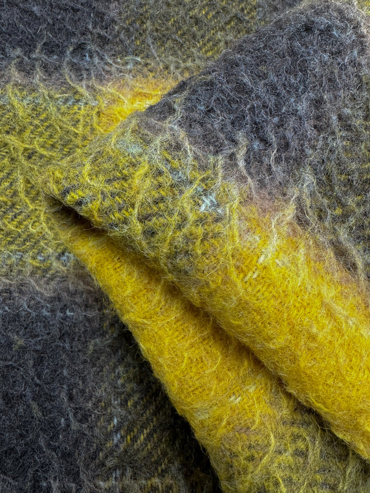 Close-up of Super Cheap Fabrics' Virgin Wool - Spruzzo - 145cm, a soft, heavy weight wool fabric featuring a gradient of yellow and gray shades. The texture appears fuzzy, showcasing the intricate fibers and the blend of colors that transitions smoothly between the hues. Perfect for overcoats, this virgin wool fabric is slightly folded.