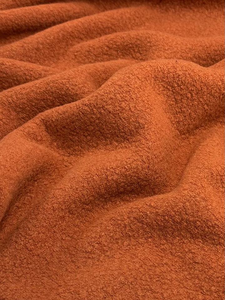 Close-up of Super Cheap Fabrics' Wool Boucle in Burnt Orange (135cm), showcasing its textured, undulating folds and slightly coarse surface that creates a wave-like pattern. Ideal for overcoats, this heavyweight fabric adds both warmth and style.