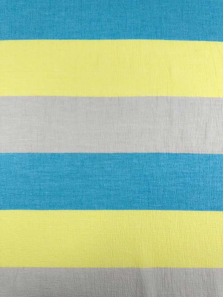 A close-up of a fabric featuring bold horizontal stripes in blue, yellow, and light gray colors. Perfect for home decor or children's clothing, this Cotton Gauze - Beachy - 130cm from Super Cheap Fabrics has a slightly rough appearance with evenly spaced stripes that create a vibrant, colorful pattern.