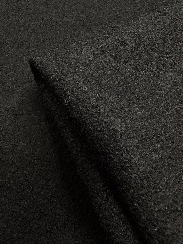Close-up of Super Cheap Fabrics' Boiled Wool - Black - 145cm, showing its dark, textured appearance. The folded material highlights its thick and dense weave, with lighting emphasizing its rich color.