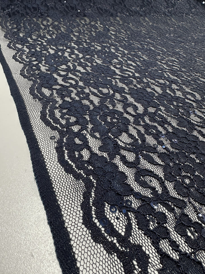 Close-up of Evening Lace - Night Sky from Super Cheap Fabrics, a black lace fabric featuring intricate floral patterns and delicate netting. The sheer lace, made from 100% polyester and measuring 145cm wide, is laid out flat, showcasing its detailed design and lightweight texture.