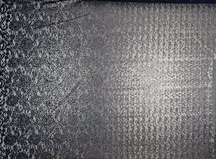 The Evening Lace - Holy Moly - 145cm by Super Cheap Fabrics features a detailed, textured surface composed of lightweight polyester. This fabric showcases an intricate, almost paisley-like pattern on the left side that gradually transitions into a more grid-like, reflective design on the right, presenting a versatile mix of dark and light tones.