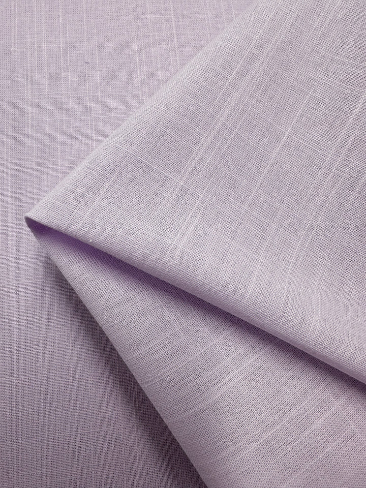 A close-up of lilac-colored linen blend fabric with a subtle texture. The lightweight fabric, neatly folded at one corner, showcases its smooth surface and fine weave. This exquisite piece from Super Cheap Fabrics is named Linen Blend - Orchid Hush - 145cm and is made in Italy.