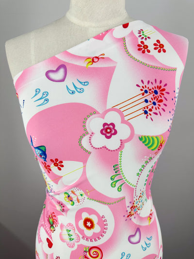 A close-up view of a mannequin showcasing a one-shoulder dress made from Super Cheap Fabrics' Printed Nylon Lycra - Anime - 158cm. The design features playful and vibrant pink and white hues with abstract shapes, flowers, hearts, and circular motifs. The soft fabric ensures comfort while enhancing the high-quality print.