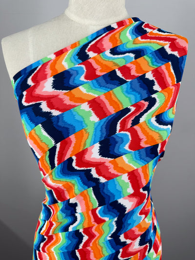 A mannequin showcases a colorful one-shoulder dress in vibrant zigzag patterns of blue, red, orange, pink, and green made from Super Cheap Fabrics' high-quality Printed Nylon Lycra - Fuzz & Waves fabric.