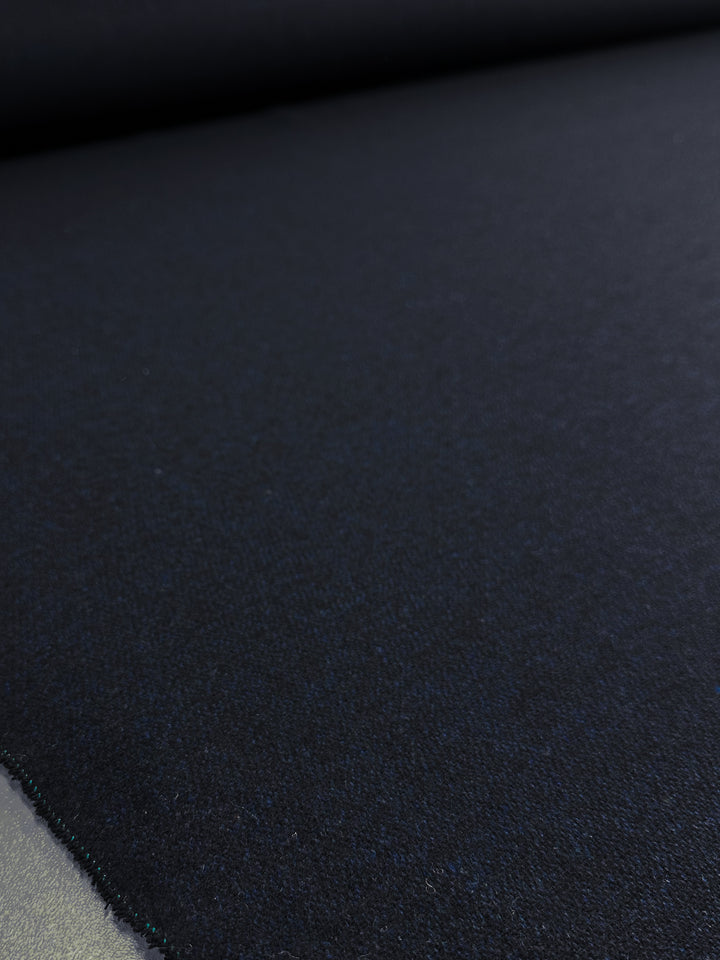A close-up of the dark-textured Wool Tweed - Vulcan (150cm) by Super Cheap Fabrics showcases its smooth, subtly shiny surface. The thick, uniform fabric shows slight color variations under light, ideal for outer coats. A softly blurred background highlights the fabric's intricate detail.