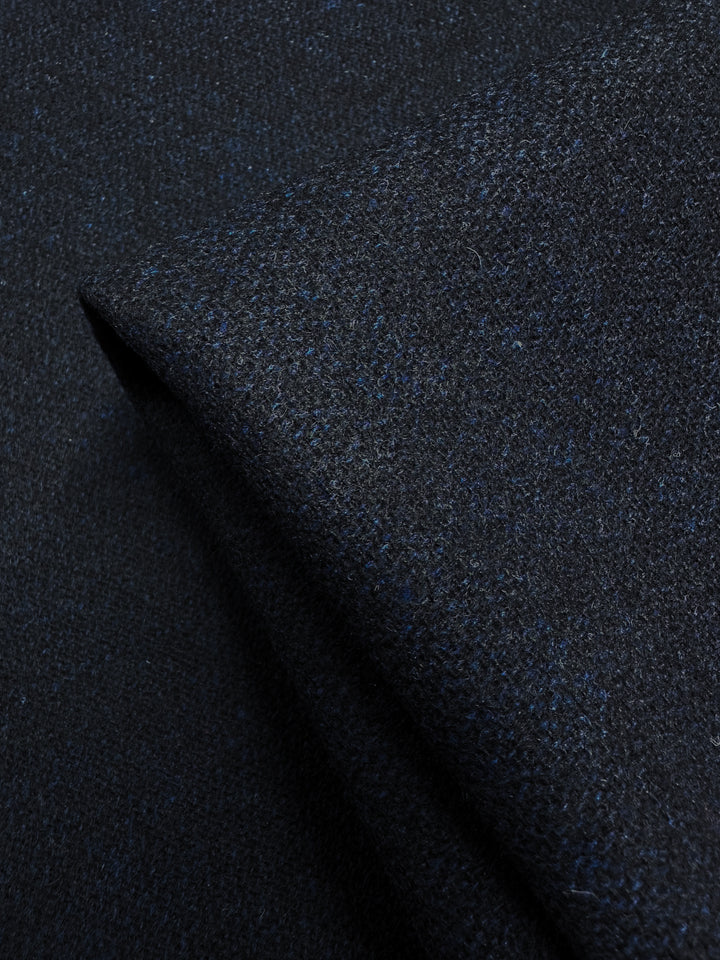 Close-up of Super Cheap Fabrics' Wool Tweed - Vulcan in dark blue, slightly folded. This 150cm fabric has fine fibers creating a soft, patterned look with subtle color variations—perfect for crafting elegant jackets or coats.