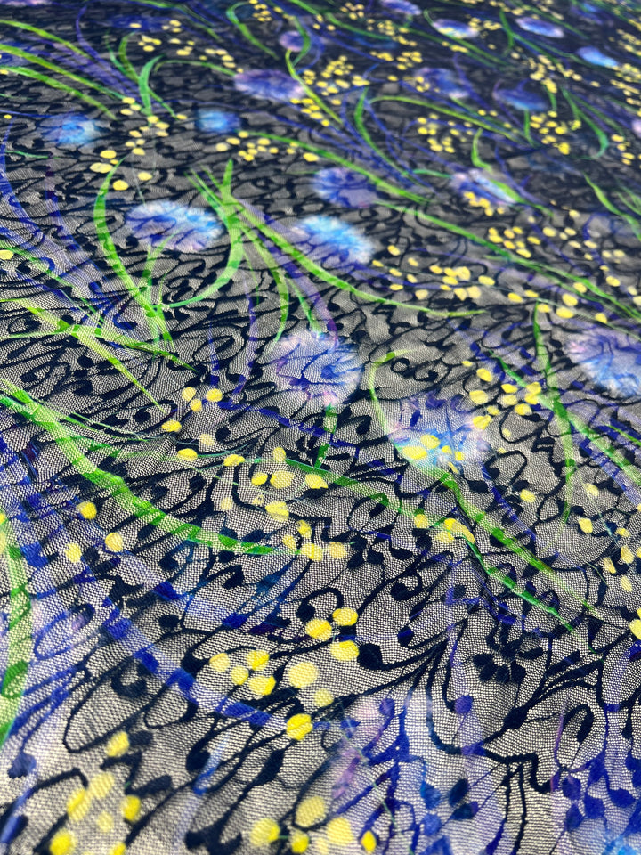 A close-up of vibrant, light weight fabric decorated with an intricate pattern. The design features swirling yellow and blue dots intertwined with green leaf-like tendrils on a dark blue background, creating an abstract, floral appearance. Made from 100% polyester, Super Cheap Fabrics’ Designer Mesh - Lotus - 150cm is perfect for multiuse projects.