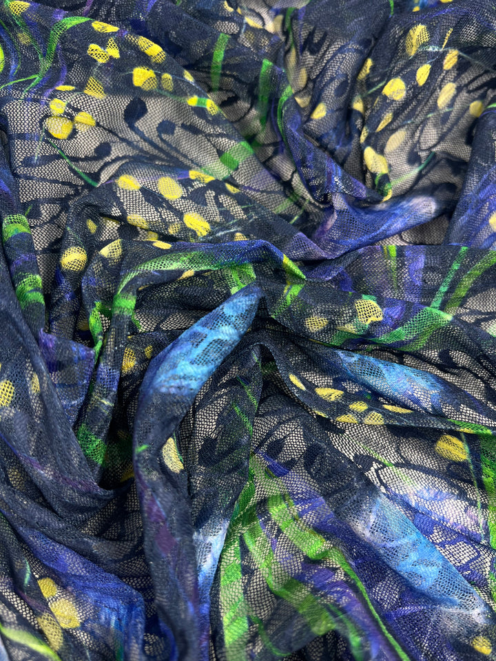 Close-up of a textured, light weight fabric with an intricate pattern. This 100% polyester material features a blend of dark blue, green, purple, and yellow hues, creating an abstract nature-inspired design. The slightly sheer texture has visible folds and layers throughout, making it perfect for multiuse applications. Introducing the Designer Mesh - Lotus - 150cm by Super Cheap Fabrics.