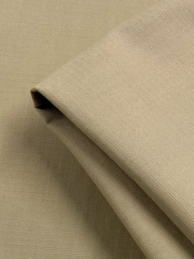 A close-up image of a beige piece of Cotton Drill - Irish Cream - 154cm from Super Cheap Fabrics, slightly folded. The texture of the fabric is smooth with a subtle, visible weave pattern.