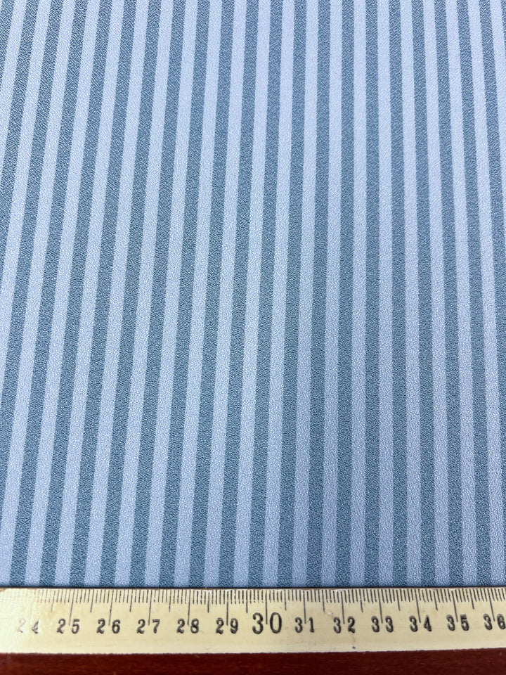 A detailed view of the Striped Crepe in Milky Blue by Super Cheap Fabrics, featuring gray stripes on polyester fabric with a measuring tape showing its 150cm width.