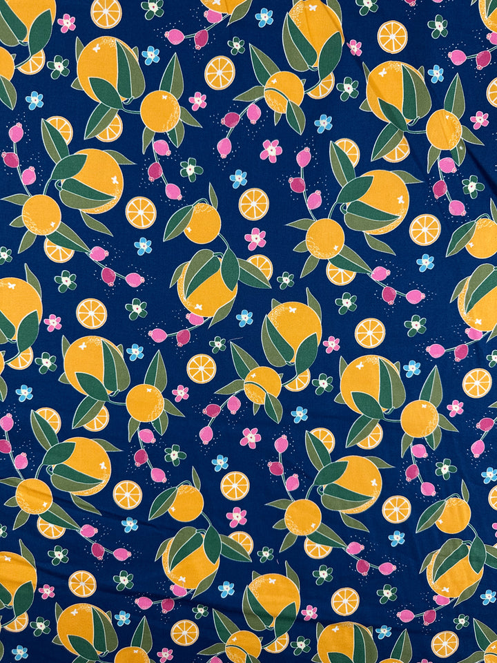 Super Cheap Fabrics’ Cotton Sateen - OJ - 145cm is a colorful medium weight fabric with whole oranges, orange slices, green leaves, radishes, and tiny flowers on dark blue—a bright and playful design.