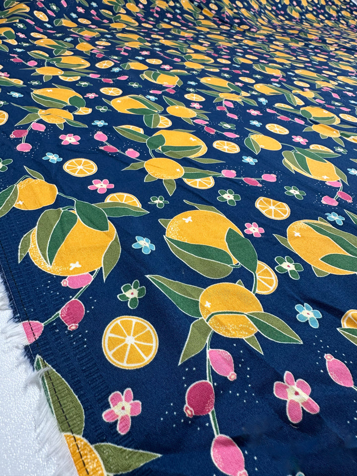 Super Cheap Fabrics' Cotton Sateen - OJ - 145cm is a navy cotton fabric with yellow lemons, green leaves, pink flowers, and orange slices—perfect for vibrant sewing projects.