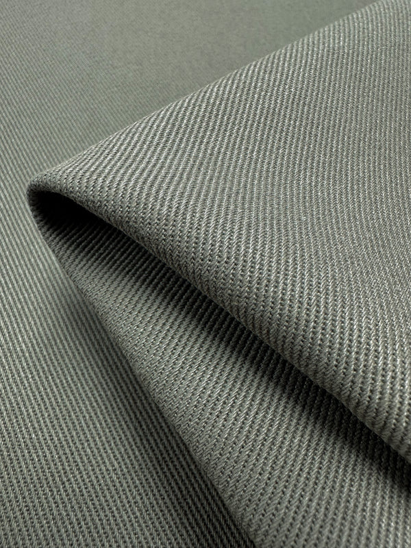 Close-up of a folded piece of Super Cheap Fabrics' Denim - Tea Leaf - 150cm, showcasing its diagonal weave pattern. The 100% cotton material has a soft texture with a subtle sheen, highlighting the intricate details of the textile weaving.