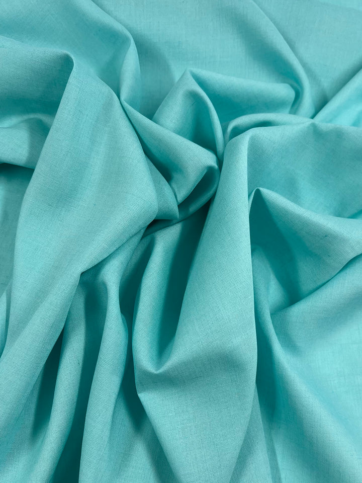 A close-up image of Pure Linen - Aquamarine - 140cm fabric with soft, flowing folds and wrinkles. The material from Super Cheap Fabrics appears to be smooth and lightweight, creating gentle curves and textures in the fabric surface.