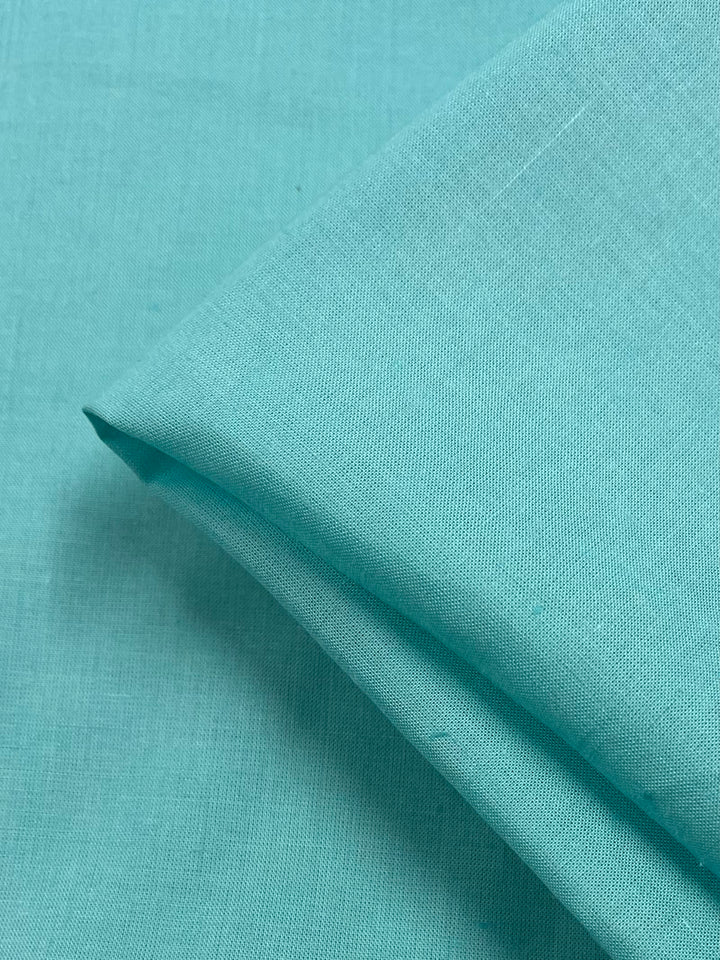 A close-up of a piece of folded Pure Linen - Aquamarine - 140cm from Super Cheap Fabrics with a subtle texture. The lightweight fabric appears smooth and neatly arranged, showcasing its vibrant color and fine weave.