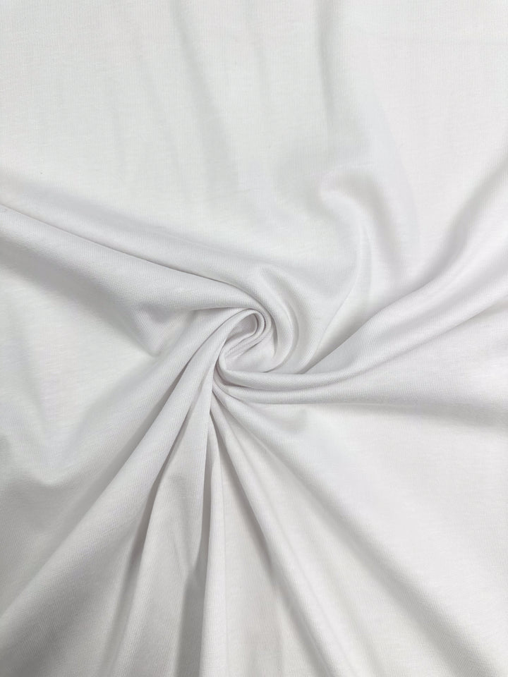 The Cotton Jersey - White from Super Cheap Fabrics, with its 175cm width, gently twists into a spiral, forming soft folds and shadows that give it a light and delicate texture reminiscent of elegant dresses.