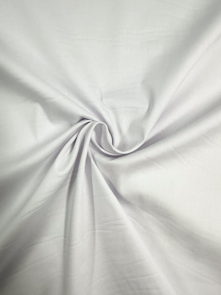 A piece of white, lightweight Stretch Cotton from Super Cheap Fabrics with a smooth texture is shown. The fabric is twisted at the center, creating a circular, swirling pattern with gentle folds radiating outward. The material appears soft and has 125 cm width.