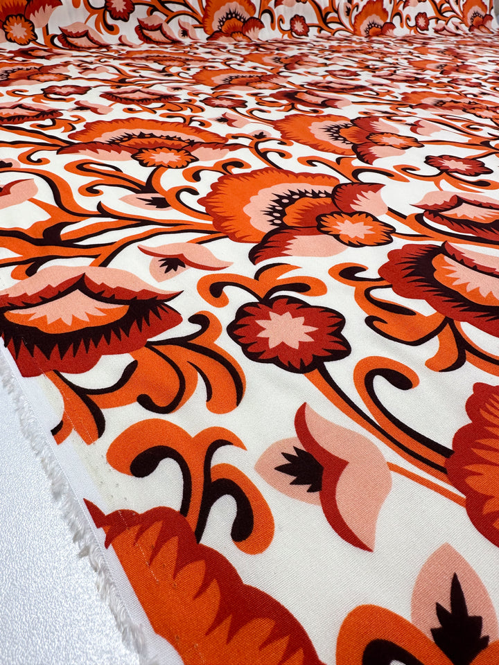 A close-up of Super Cheap Fabrics' Designer Rayon - Floral Delight - 145cm shows vibrant, retro orange, red, and pink florals on white—perfect for versatile clothing with bold prints.